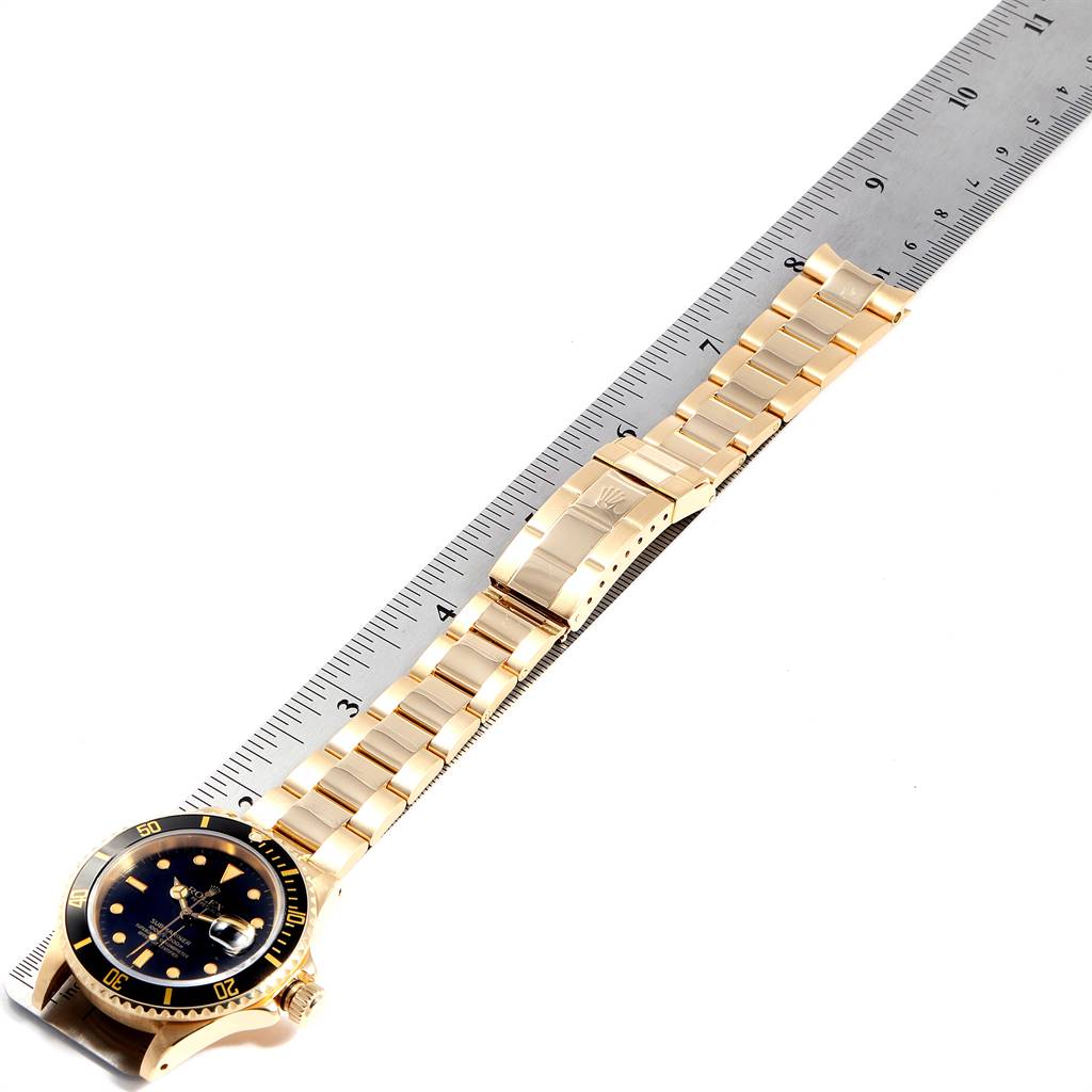 The image shows a Rolex Submariner 16618 Men
s Yellow Gold Black Dial 16618 Men
s Yellow Gold Black Dial watch laid flat next to a ruler, displaying the watch face, bracelet, and clasp.