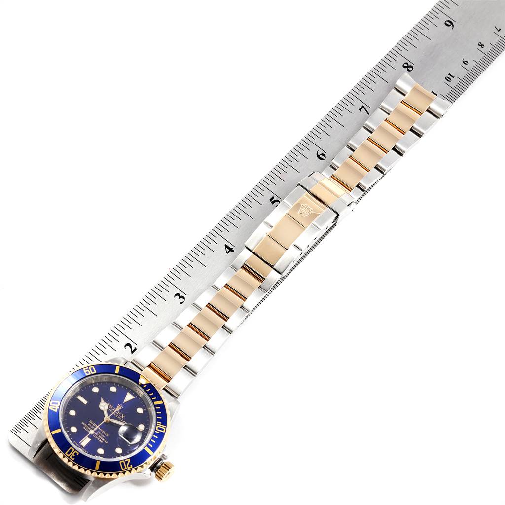 The Rolex Submariner 16613 Men
s Steel and Gold (two tone) Blue Dial 16613 Men
s Steel and Gold (two tone) Blue Dial watch is shown from a top-down angle with its entire bracelet placed alongside a ruler.