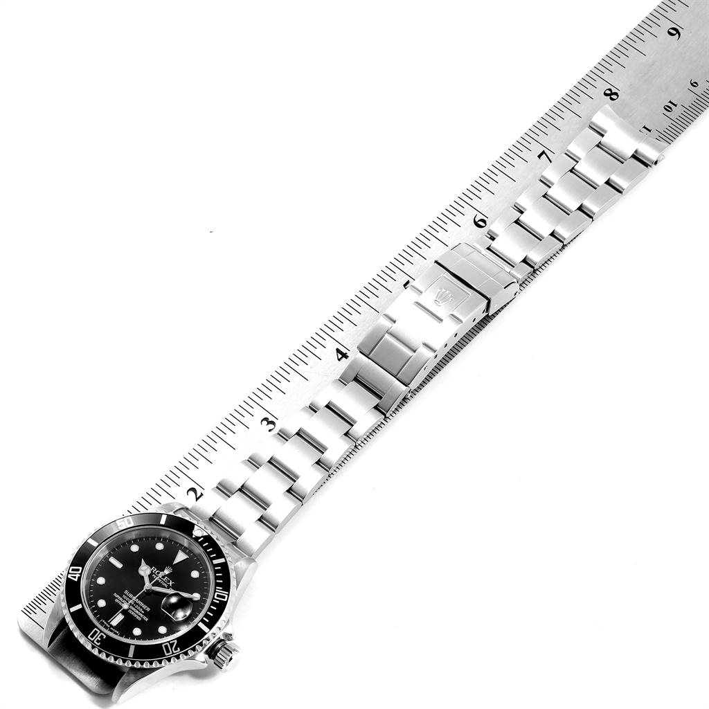 The image shows a Rolex Submariner 16610 Men
s Stainless Steel Black Dial 16610 Men
s Stainless Steel Black Dial watch laid flat on a ruler, highlighting the dial, bezel, and bracelet.
