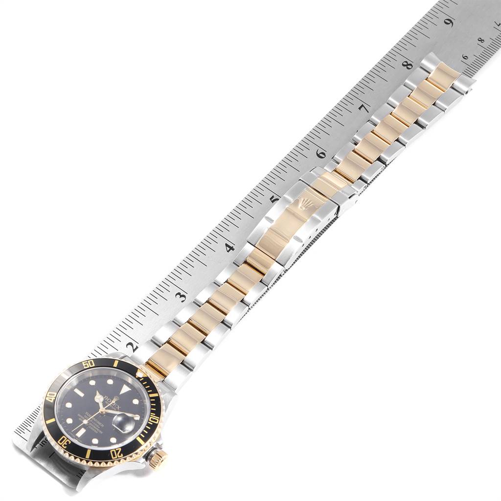 The image shows a Rolex Submariner 16613 Men's Steel and Gold (two tone) Black Dial 16613 Men's Steel and Gold (two tone) Black Dial watch laid flat with its bracelet measured against a ruler, highlighting the face, bezel, and band.