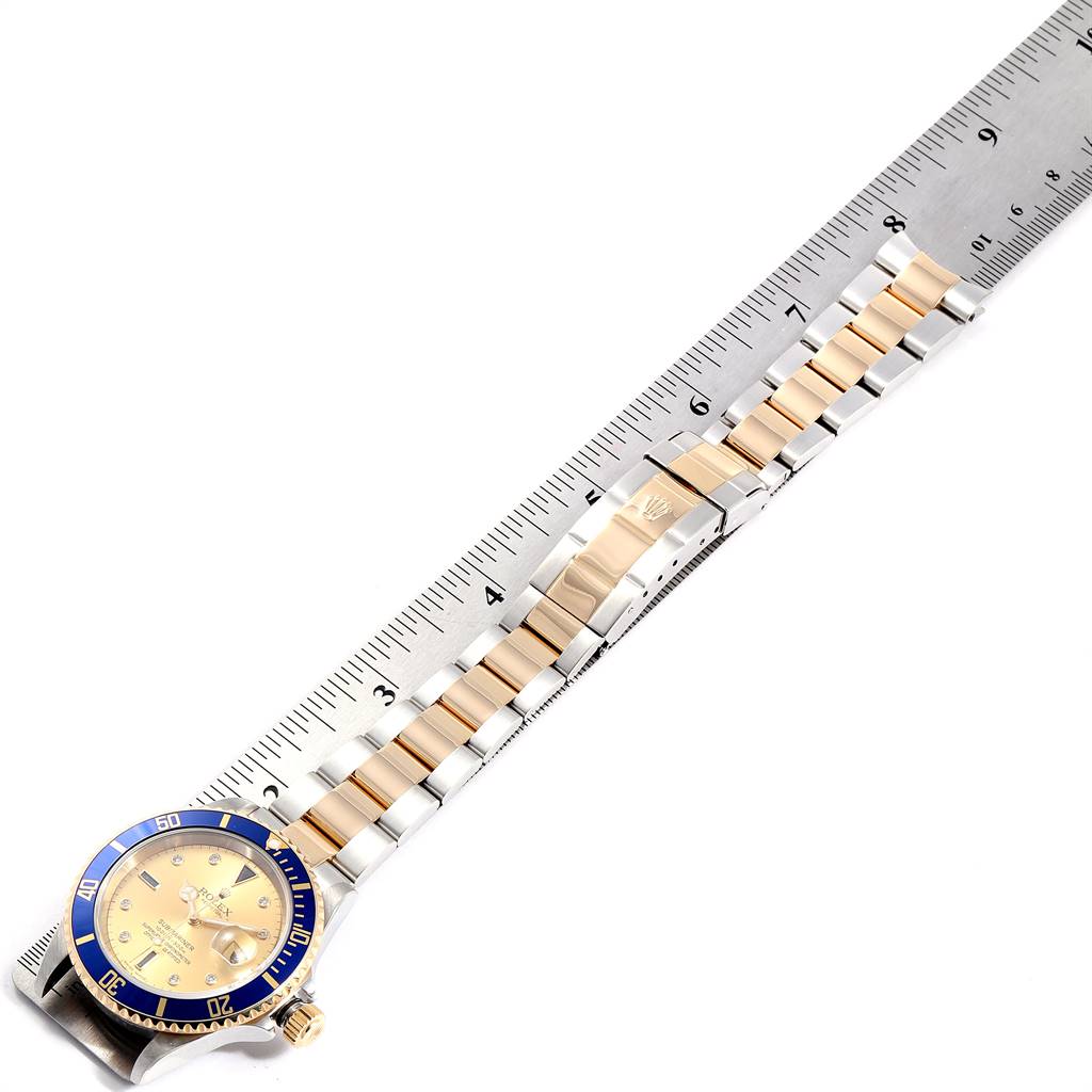 This image shows a top view of a Rolex Submariner 16613 Men
s Steel and Gold (two tone) Champagne Dial 16613 Men
s Steel and Gold (two tone) Champagne Dial watch with a two-tone metal bracelet next to a ruler.