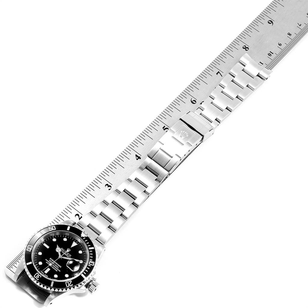 The image shows a Rolex Submariner 16610 Men
s Stainless Steel Black Dial 16610 Men
s Stainless Steel Black Dial watch laid flat next to a ruler, highlighting the watch face and bracelet.