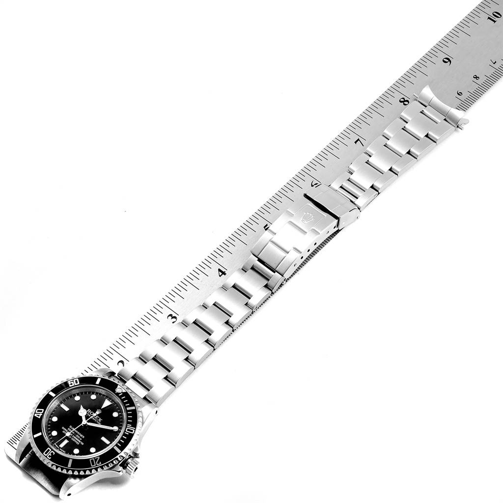 The image shows a Rolex Submariner 14060M Men
s Stainless Steel Black Dial 14060M Men
s Stainless Steel Black Dial watch laid flat against a ruler, highlighting the bracelet and clasp.