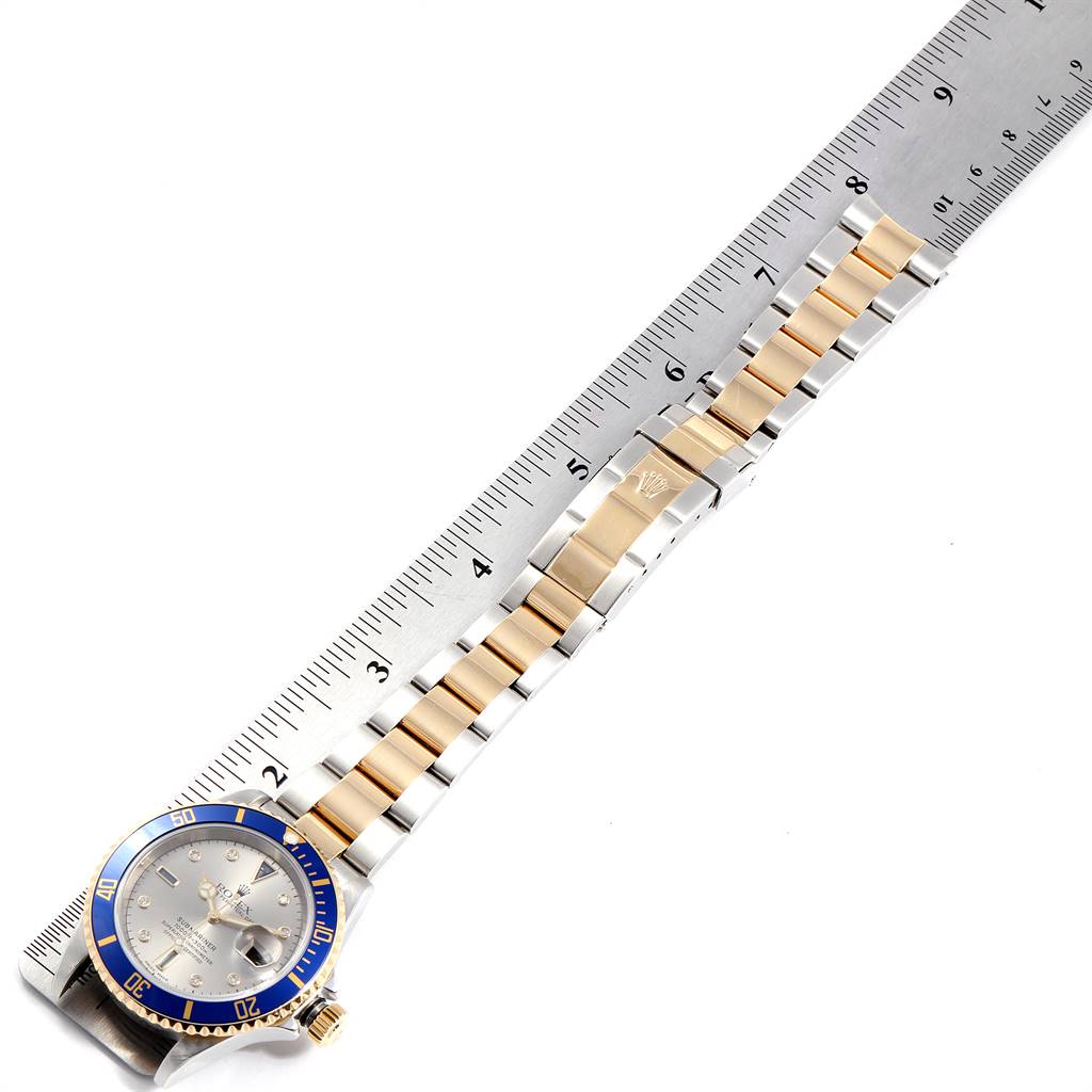 The Rolex Submariner 16613 Men
s Steel and Gold (two tone) Grey Dial 16613 Men
s Steel and Gold (two tone) Grey Dial watch is shown flat with its two-tone band fully extended next to a measuring ruler.