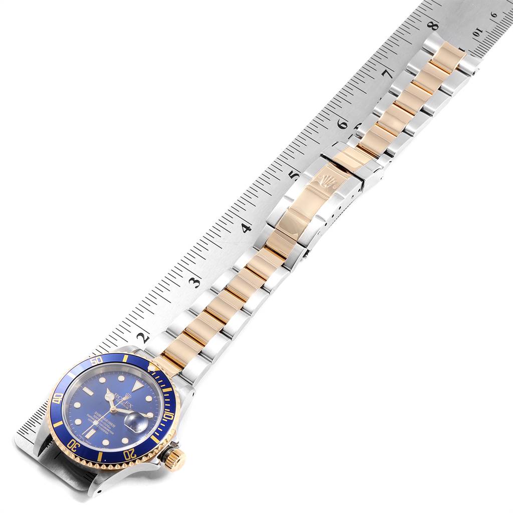 The image shows a Rolex Submariner 16613 Men
s Steel and Gold (two tone) Blue Dial 16613 Men
s Steel and Gold (two tone) Blue Dial watch lying flat with its band and clasp measured against a ruler.