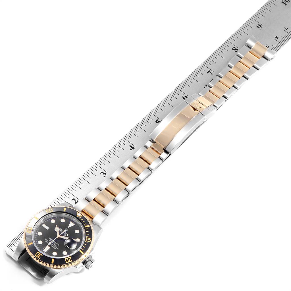 The image shows a Rolex Submariner 116613 Men
s Steel and Gold (two tone) Black Dial 116613 Men
s Steel and Gold (two tone) Black Dial watch positioned diagonally on a ruler, highlighting the case, bezel, dial, and bracelet.