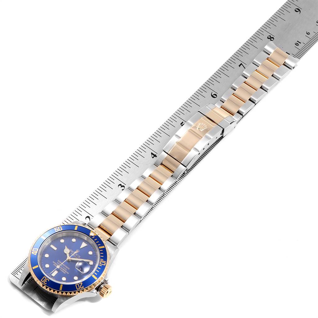 The Rolex Submariner 16613 Men
s Steel and Gold (two tone) Blue Dial 16613 Men
s Steel and Gold (two tone) Blue Dial watch is displayed flat, showing the face, bracelet, and clasp next to a ruler for size reference.