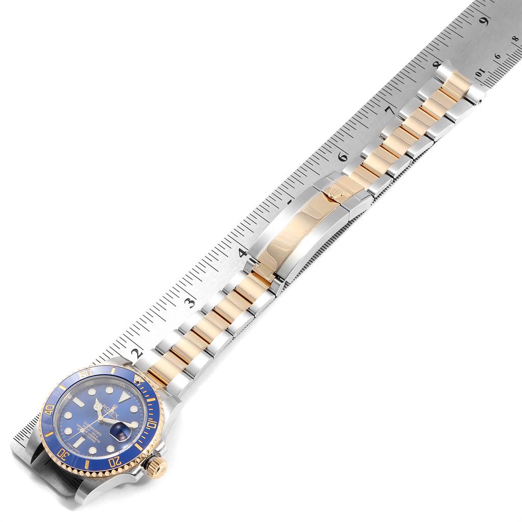 The image shows a Rolex Submariner 116613 Men
s Steel and Gold (two tone) Blue Dial 116613 Men
s Steel and Gold (two tone) Blue Dial watch laid flat against a ruler, displaying its face, bezel, and bracelet fully extended.