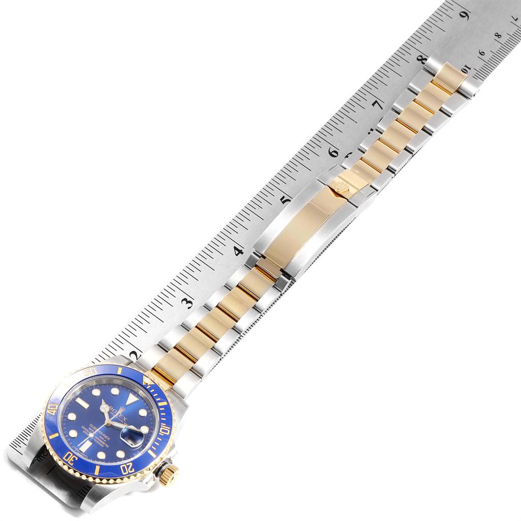 The image shows a blue Rolex Submariner 116613 Men
s Steel and Gold (two tone) Blue Dial 116613 Men
s Steel and Gold (two tone) Blue Dial laid flat against a ruler, displaying the face and entire bracelet.
