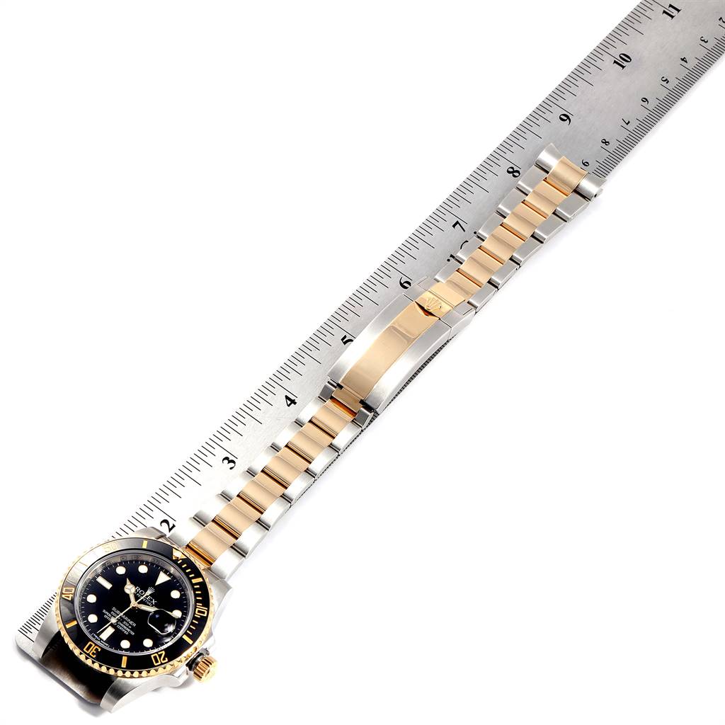 The image shows a Rolex Submariner 116613 Men
s Steel and Gold (two tone) Black Dial 116613 Men
s Steel and Gold (two tone) Black Dial watch laid flat next to a ruler, displaying its entire bracelet and face.