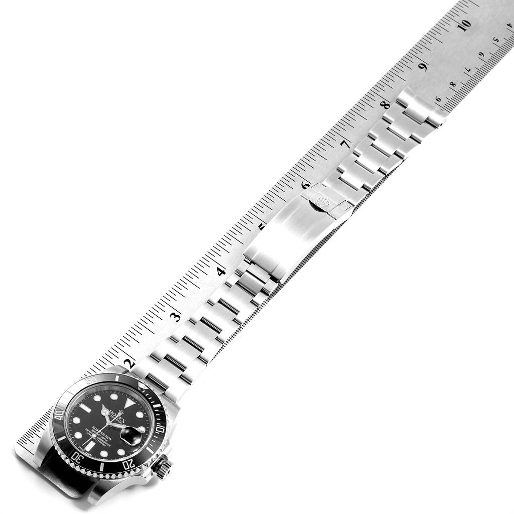 The image shows a Rolex Submariner 116610 Men
s Stainless Steel Black Dial 116610 Men
s Stainless Steel Black Dial watch laid flat, alongside a ruler, with its face, bracelet, and clasp visible.