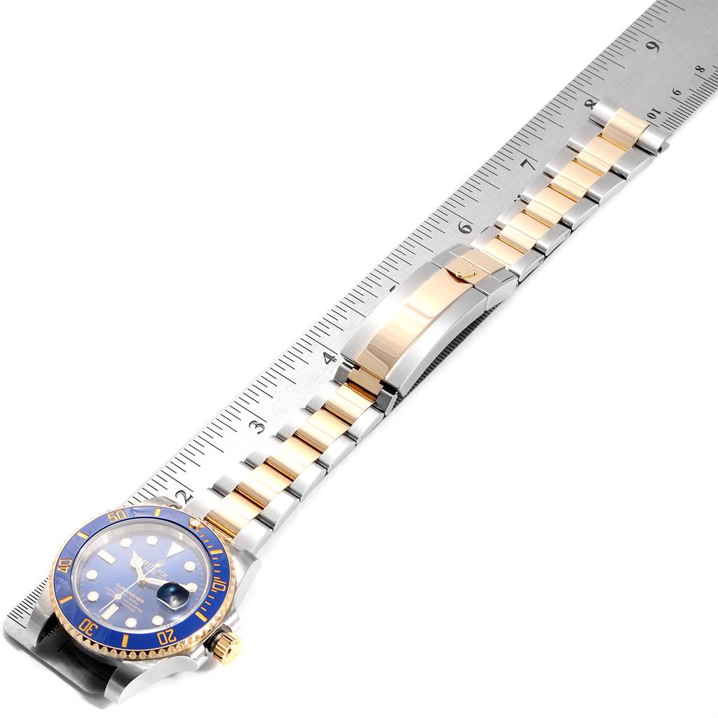 The image shows a Rolex Submariner 116613 Men
s Steel and Gold (two tone) Blue Dial 116613 Men
s Steel and Gold (two tone) Blue Dial watch at an angled top-down view, displaying the face, bezel, and bracelet alongside a ruler for scale.