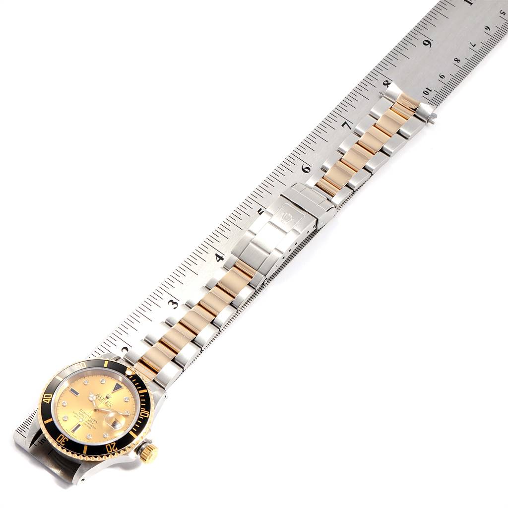 The image shows a Rolex Submariner 16613 Men
s Steel and Gold (two tone) Champagne Dial 16613 Men
s Steel and Gold (two tone) Champagne Dial watch laid flat, highlighting its bracelet and clasp against a ruler for scale.