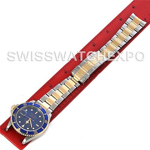 The angle shows the top view of the Rolex Submariner 16613 Men's Yellow Gold Blue Dial 16613 Men's Yellow Gold Blue Dial watch, including its blue dial, bezel, and two-tone bracelet on a red ruler.