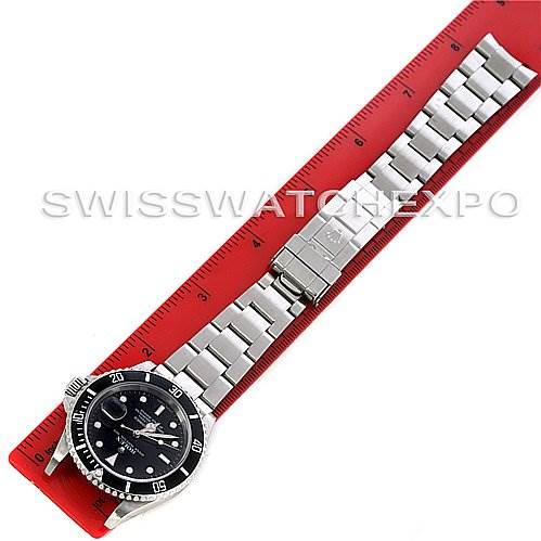 The image shows a Rolex Submariner 16610 Men
s Stainless Steel Black Dial 16610 Men
s Stainless Steel Black Dial watch laid flat alongside a red measuring ruler.