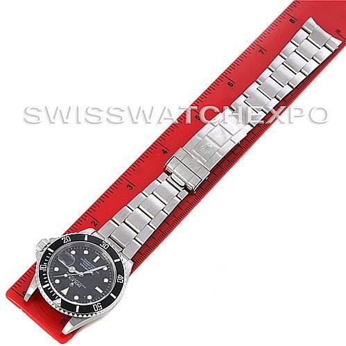 This image shows a top-down view of a Rolex Submariner 16610 Men
s Stainless Steel Black Dial 16610 Men
s Stainless Steel Black Dial watch and its metal bracelet placed on a red ruler.