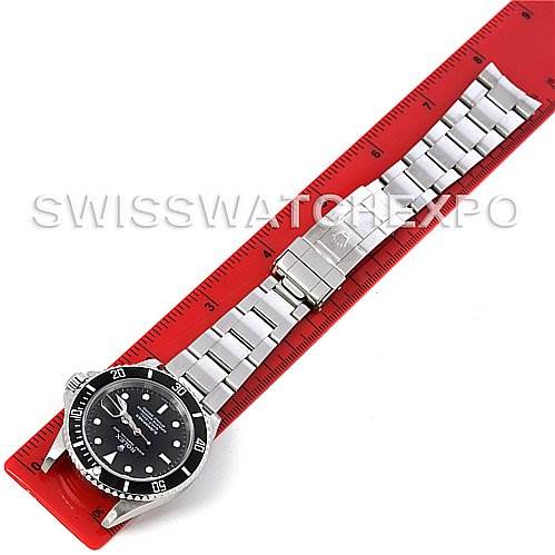 The image shows a Rolex Submariner 16610 Men
s Stainless Steel Black Dial 16610 Men
s Stainless Steel Black Dial watch laid flat, displaying the full bracelet and face, positioned on a red ruler.