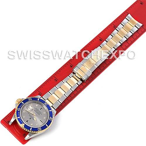 This image shows a Rolex Submariner 16613 Men's Steel and Gold (two tone) Grey Dial 16613 Men's Steel and Gold (two tone) Grey Dial watch laid flat, with a focus on its bracelet and bezel, placed on a red measuring ruler.