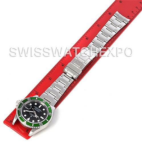 The image shows a Rolex Submariner 16610T Men's Stainless Steel Black Dial 16610T Men's Stainless Steel Black Dial watch laid flat, with its green bezel, dial, and metal bracelet fully visible against a red ruler.