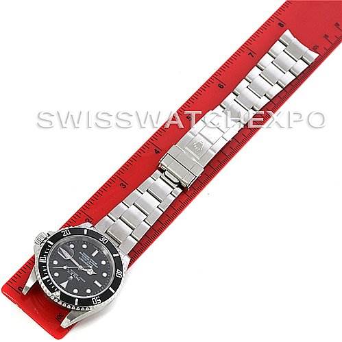 The Rolex Submariner 16610T Men's Stainless Steel Black Dial 16610T Men's Stainless Steel Black Dial watch is shown from a top-down angle on a red ruler, displaying the face and bracelet.
