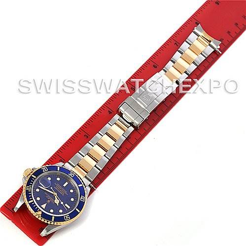 This image shows a top-down view of a Rolex Submariner 16613 Men's Steel and Gold (two tone) Blue Dial 16613 Men's Steel and Gold (two tone) Blue Dial watch placed on a red ruler.