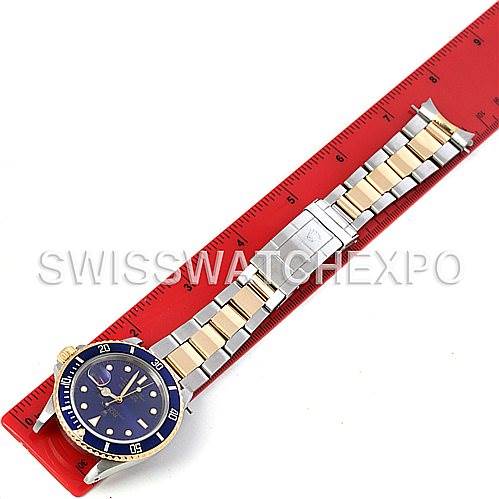 This image shows a Rolex Submariner 16803 Men's Steel and Gold (two tone) Blue Dial 16803 Men's Steel and Gold (two tone) Blue Dial watch laid flat next to a red ruler, displaying the full bracelet and dial.