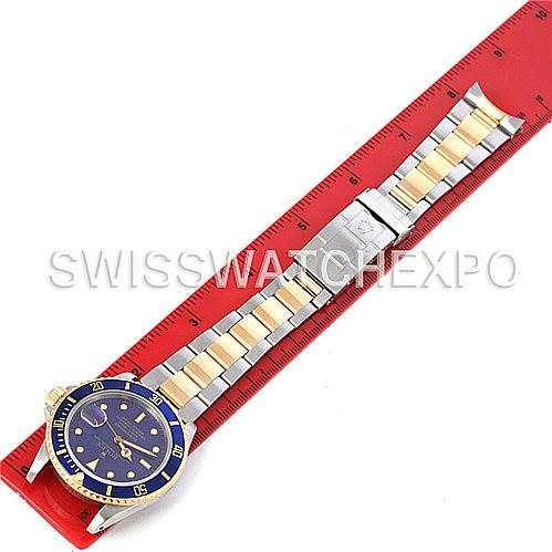 The image shows a top-down view of a Rolex Submariner 16803 Men's Steel and Gold (two tone) Blue Dial 16803 Men's Steel and Gold (two tone) Blue Dial watch with a two-tone bracelet placed next to a red ruler.