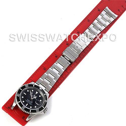 The image shows a top-view angle of the Rolex Submariner 16610 Men's Stainless Steel Black Dial 16610 Men's Stainless Steel Black Dial watch with a stainless steel bracelet on a red ruler.