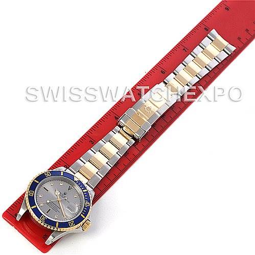 The image shows a top-down view of a Rolex Submariner 16613 Men's Steel and Gold (two tone) Grey Dial 16613 Men's Steel and Gold (two tone) Grey Dial watch, highlighting the face, bezel, and bracelet laid on a measuring scale.