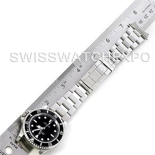 The Rolex Submariner 14060M Men's Stainless Steel Black Dial 14060M Men's Stainless Steel Black Dial watch is shown from a top-down angle, displaying the face, bezel, and bracelet beside a ruler.