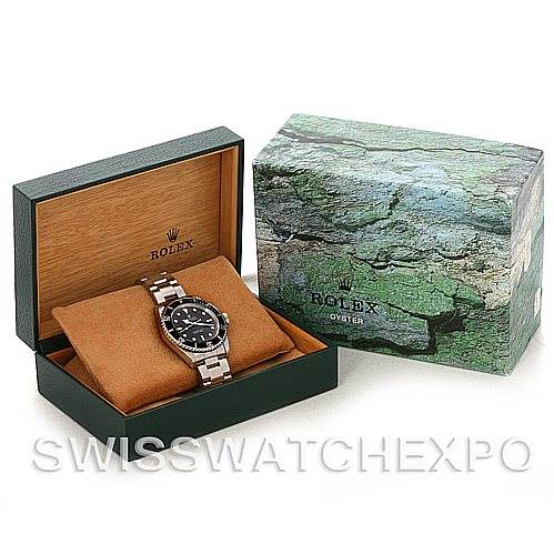 The image shows a Rolex Submariner 14060M Men's Stainless Steel Black Dial 14060M Men's Stainless Steel Black Dial watch from a front angle, placed in an open green and tan watch box, with its detailed exterior packaging.