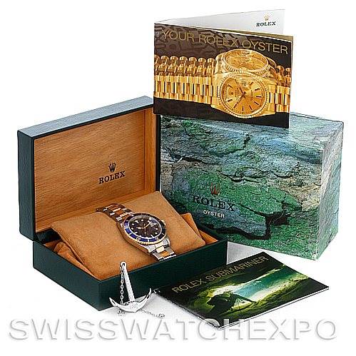 A Rolex Submariner 16613 Men's Steel and Gold (two tone) Blue Dial 16613 Men's Steel and Gold (two tone) Blue Dial watch is displayed in its open box, accompanied by brochures and an anchor accessory.