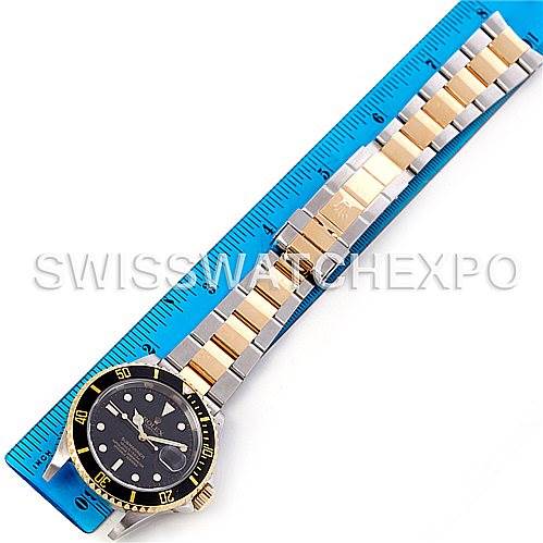 The image shows a Rolex Submariner 16613 Men's Steel and Gold (two tone) Black Dial 16613 Men's Steel and Gold (two tone) Black Dial watch laid flat with its two-tone gold and stainless steel bracelet fully extended alongside a ruler.