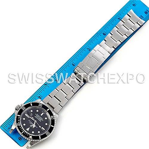 The Rolex Submariner 16610 Men's Stainless Steel Black Dial 16610 Men's Stainless Steel Black Dial watch is shown laid flat next to a blue ruler, highlighting its full bracelet and face from an overhead angle.