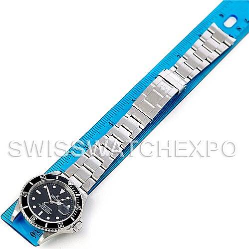 The image shows a top-down view of a Rolex Submariner 16610 Men
s Stainless Steel Black Dial 16610 Men
s Stainless Steel Black Dial with its metal bracelet extended and aligned with a blue ruler for measurement.