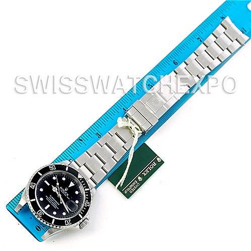 The image shows a Rolex Submariner 16610 Men's Stainless Steel Black Dial 16610 Men's Stainless Steel Black Dial watch laid flat against a blue ruler, displaying the dial, bezel, bracelet, and tag.