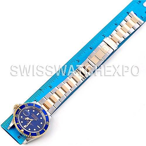 The image shows a full-length view of a Rolex Submariner 16613 Men's Steel and Gold (two tone) Blue Dial 16613 Men's Steel and Gold (two tone) Blue Dial watch, placed next to a blue measuring ruler.