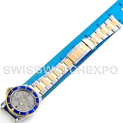 This image shows a top view of a Rolex Submariner 16613 Men's Steel and Gold (two tone) Grey Dial 16613 Men's Steel and Gold (two tone) Grey Dial watch laying flat beside a blue ruler, highlighting its bracelet and watch face.