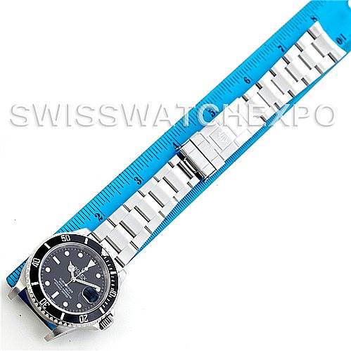 The image shows a Rolex Submariner 16610 Men
s Stainless Steel Black Dial 16610 Men
s Stainless Steel Black Dial watch laid flat next to a blue ruler, displaying the watch’s face and bracelet.