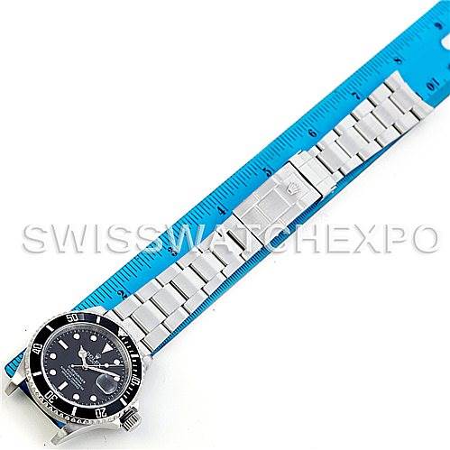 The image shows a Rolex Submariner 16610 Men
s Stainless Steel Black Dial 16610 Men
s Stainless Steel Black Dial watch laid flat next to a blue ruler, displaying the watch face and entire metal band.