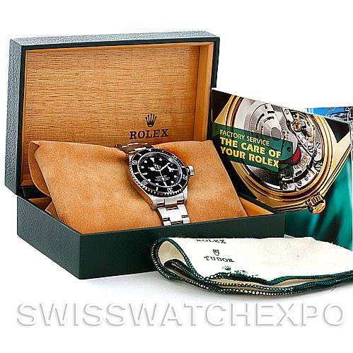 The image shows a Rolex Submariner 16610 Men
s Stainless Steel Black Dial 16610 Men
s Stainless Steel Black Dial watch at an angle inside an open box, accompanied by a booklet and cleaning cloth.