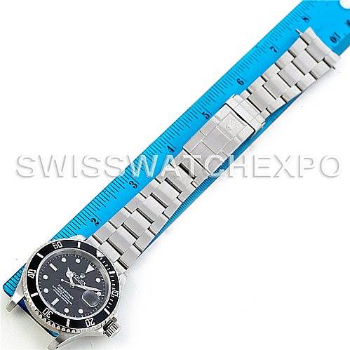 The image shows a side view of a Rolex Submariner 16610 Men
s Stainless Steel Black Dial 16610 Men
s Stainless Steel Black Dial watch laid next to a blue ruler, capturing the watch face and entire bracelet.