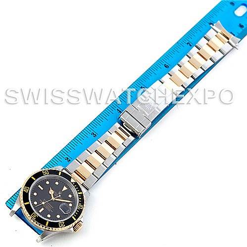 The image shows a Rolex Submariner 16613 Men
s Steel and Gold (two tone) Black Dial 16613 Men
s Steel and Gold (two tone) Black Dial watch laid flat against a blue ruler, highlighting its full bracelet and watch face from an overhead angle.