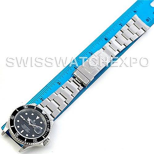 The Rolex Submariner 16610 Men
s Stainless Steel Black Dial 16610 Men
s Stainless Steel Black Dial watch is shown from a top-down angle, displaying the face, bezel, and full metal bracelet next to a blue ruler.