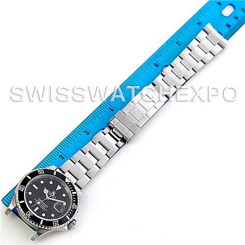 The image shows a Rolex Submariner 16610 Men
s Stainless Steel Black Dial 16610 Men
s Stainless Steel Black Dial watch laid flat with its full bracelet extended alongside a blue ruler.