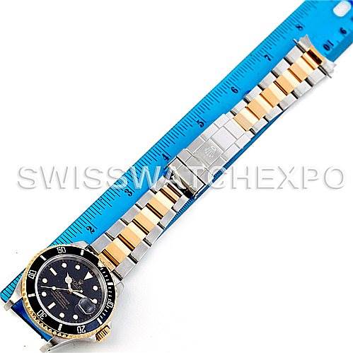 The Rolex Submariner 16613 Men's Steel and Gold (two tone) Black Dial 16613 Men's Steel and Gold (two tone) Black Dial watch is shown laid flat next to a blue ruler, displaying the face and bracelet from a top-down angle.
