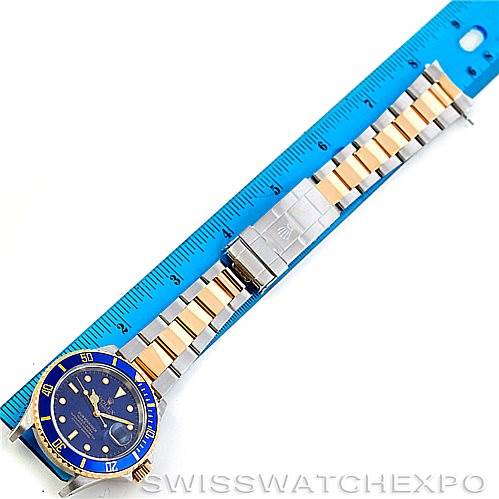 The image shows a Rolex Submariner 16613 Men's Steel and Gold (two tone) Blue Dial 16613 Men's Steel and Gold (two tone) Blue Dial watch laid flat next to a blue ruler, displaying the full bracelet and face.
