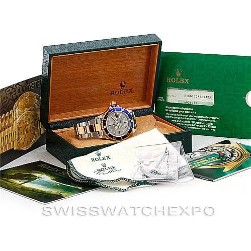 The Rolex Submariner 16613 Men
s Steel and Gold (two tone) Grey Dial 16613 Men
s Steel and Gold (two tone) Grey Dial watch is shown from the front inside an open box, along with its booklet, warranty card, and cleaning cloth.