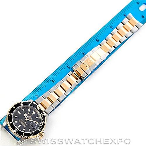 The image shows a Rolex Submariner 16613 Men's Steel and Gold (two tone) Black Dial 16613 Men's Steel and Gold (two tone) Black Dial watch with its full length and bracelet placed against a blue ruler for scale.