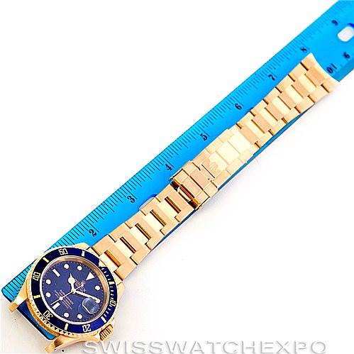 This image shows a top-down view of a Rolex Submariner 16618 Men's Yellow Gold Blue Dial 16618 Men's Yellow Gold Blue Dial watch with its bracelet aligned next to a blue ruler.